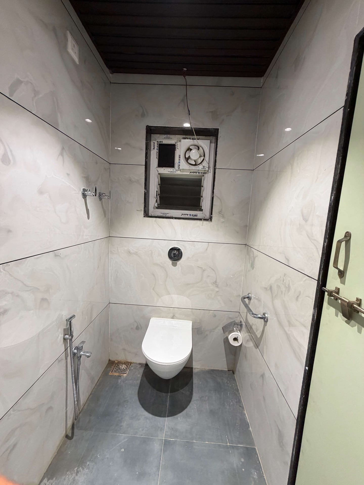 Marble-tiled bathroom with shower mixer, wall-hung WC, grab rail and ventilation window