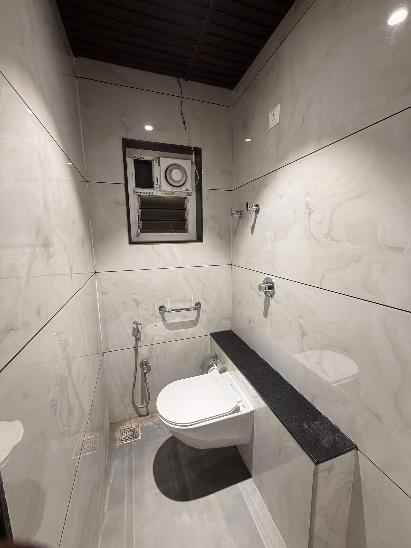 En-suite bathroom clad floor to ceiling in white marble-effect tile with a wall-hung WC, health faucet and granite ledge