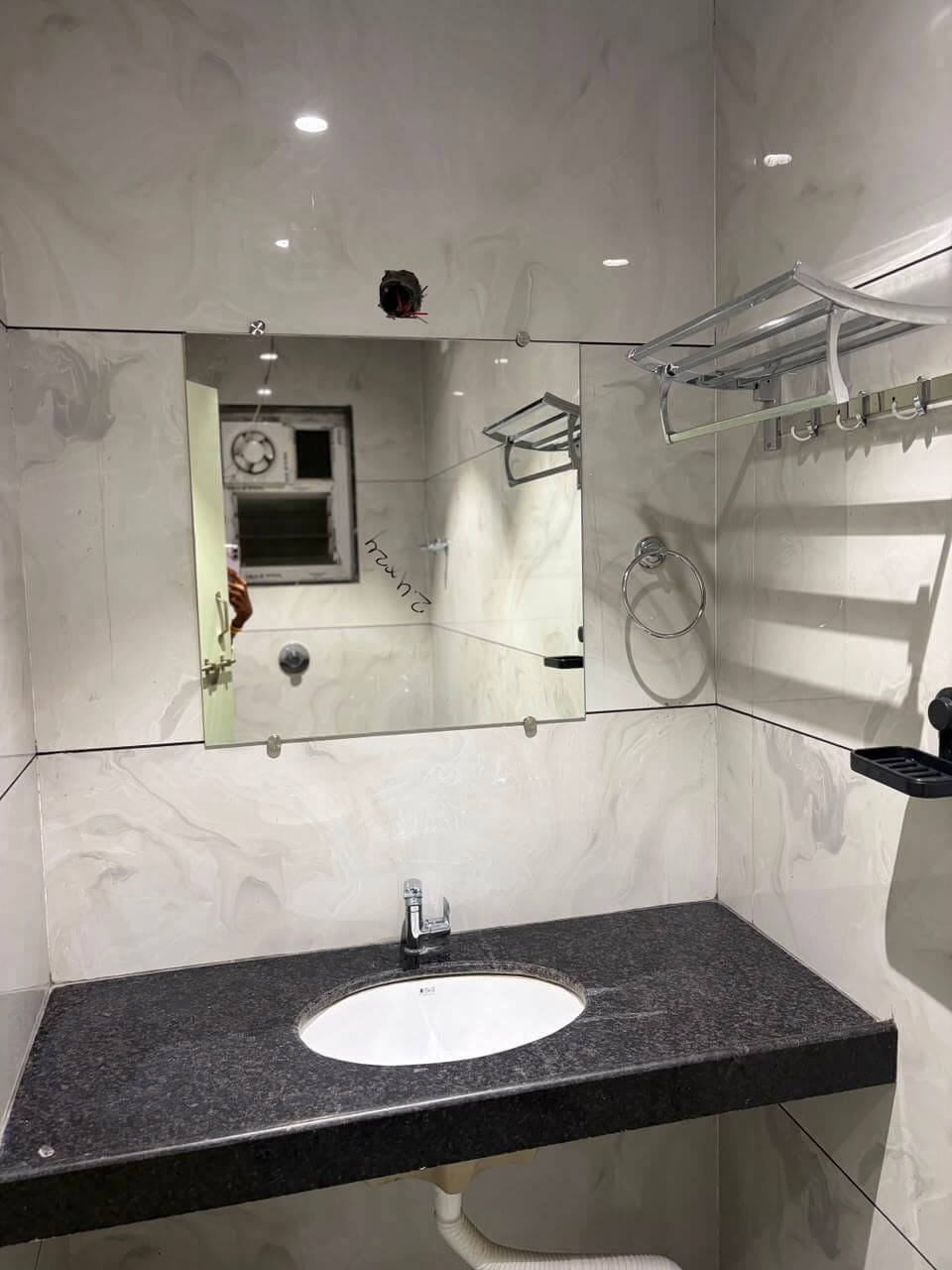 Bathroom vanity with a granite counter, undermount basin, wide mirror, towel rail and chrome shelf against marble-effect tile