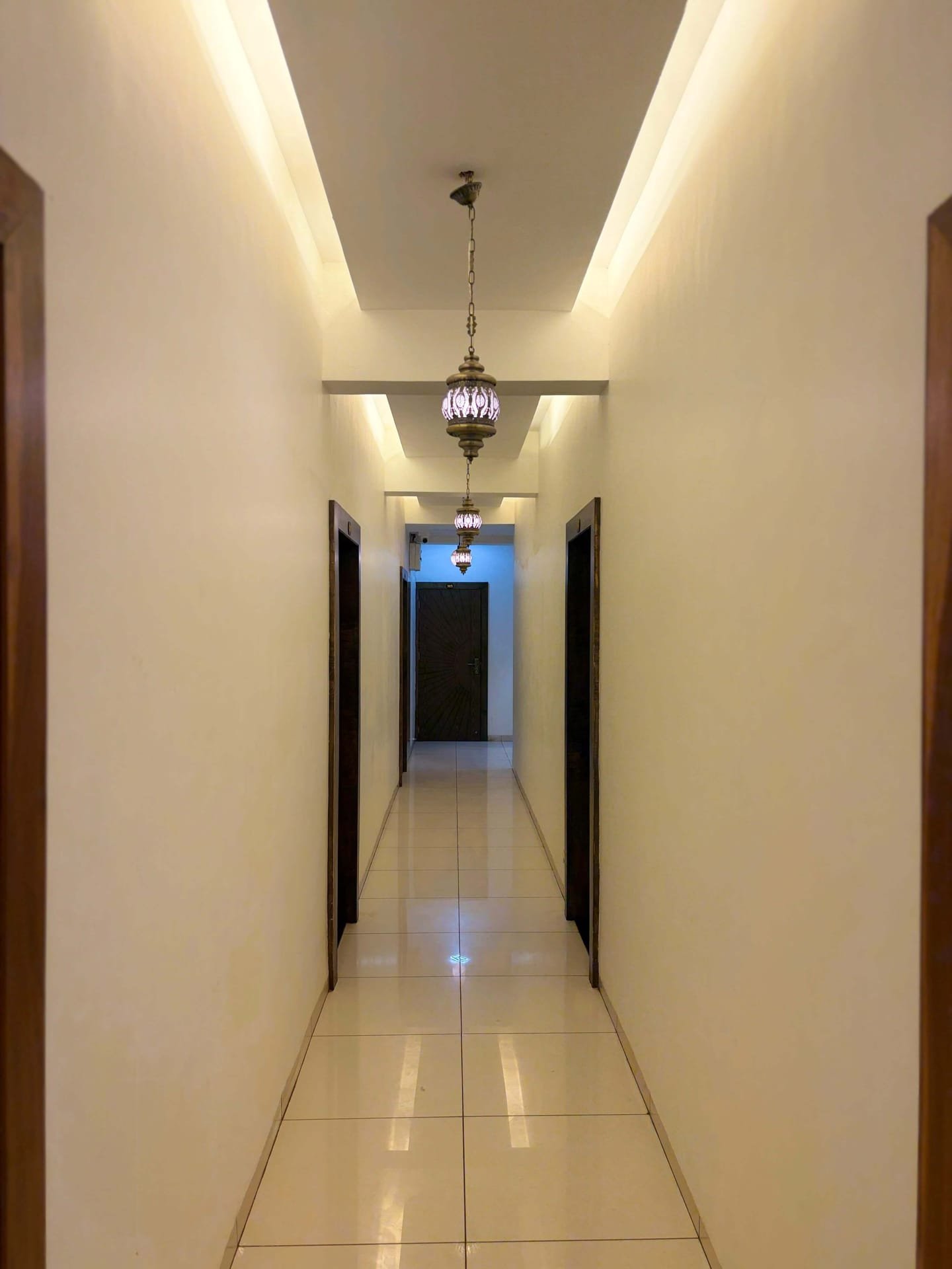 Guest-floor corridor with polished cream tiles, dark timber doors and a row of hanging metal lanterns