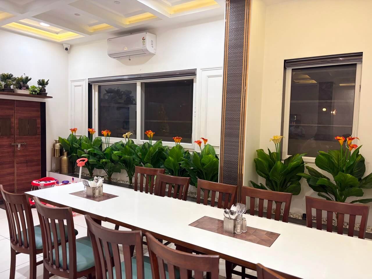 Family-style long dining table with cutlery stands, flanked by planters of foliage and calla lilies
