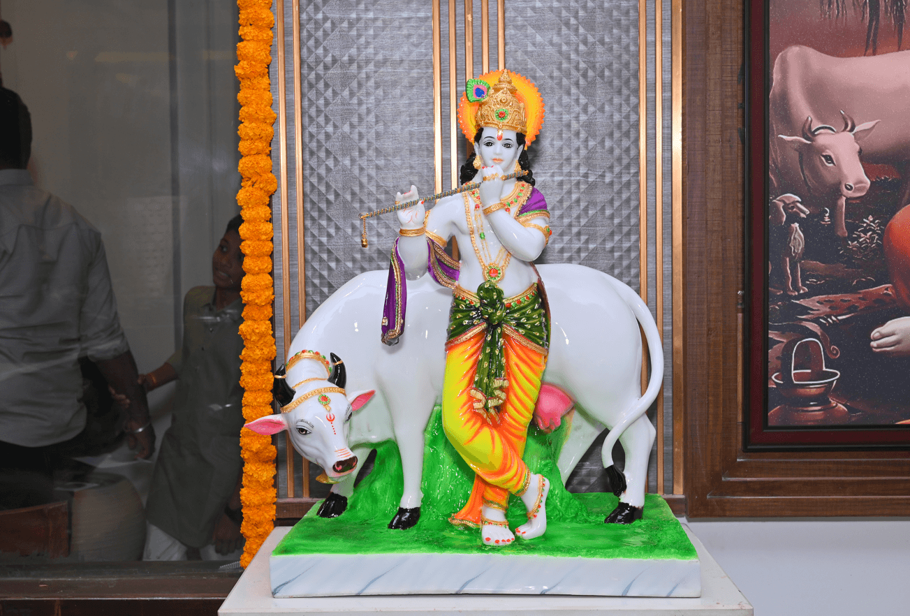 Marble idol of Krishna with a cow, framed by a marigold garland on the wall behind
