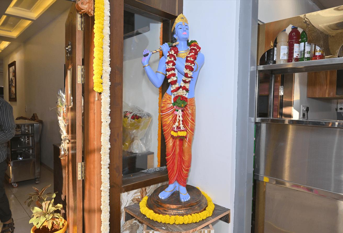 Standing Krishna idol playing the flute, garlanded with marigolds beside the carved timber entrance doors