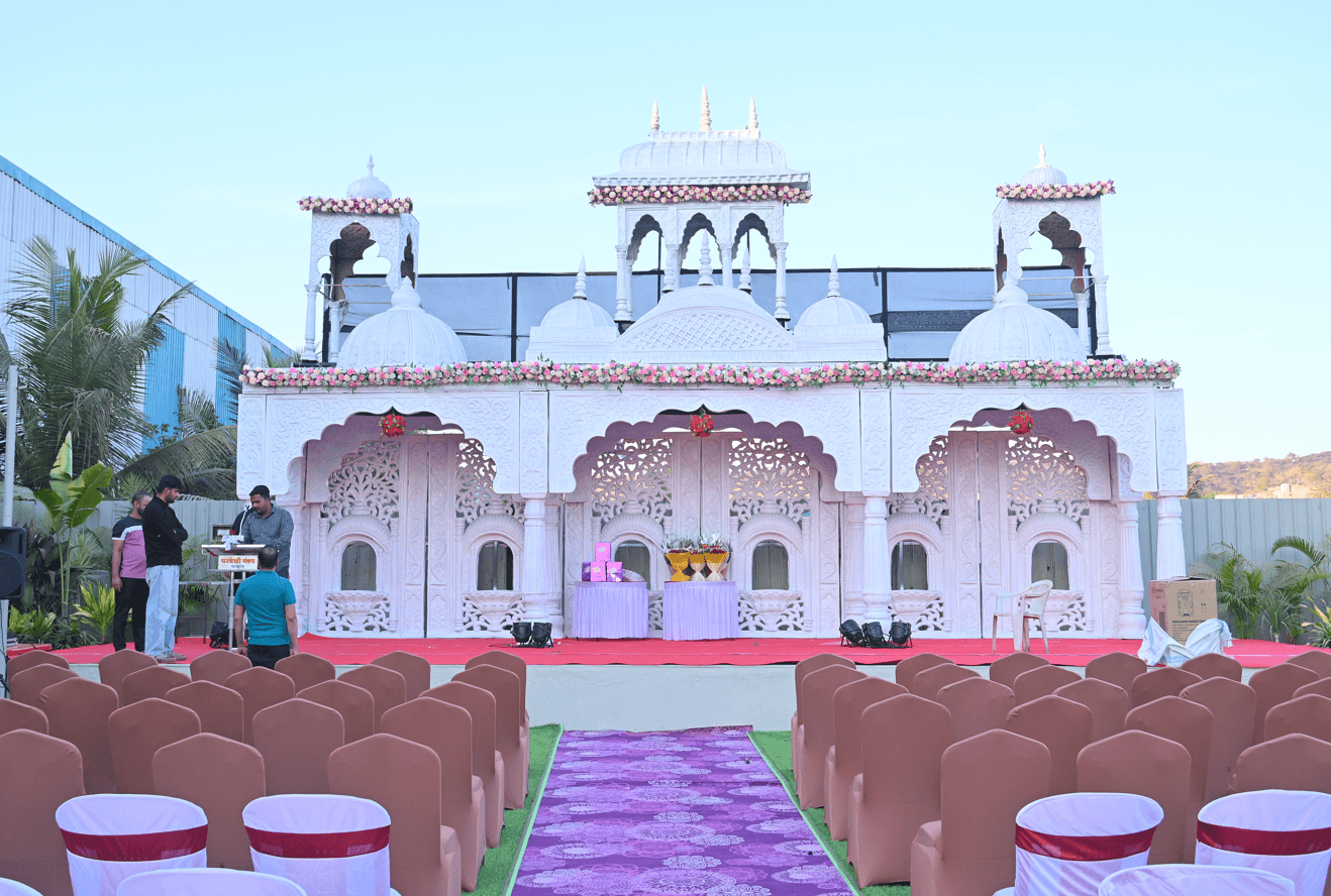 Ornate white mandap with carved arches and domes on the open-air lawn, dressed with pink and white florals