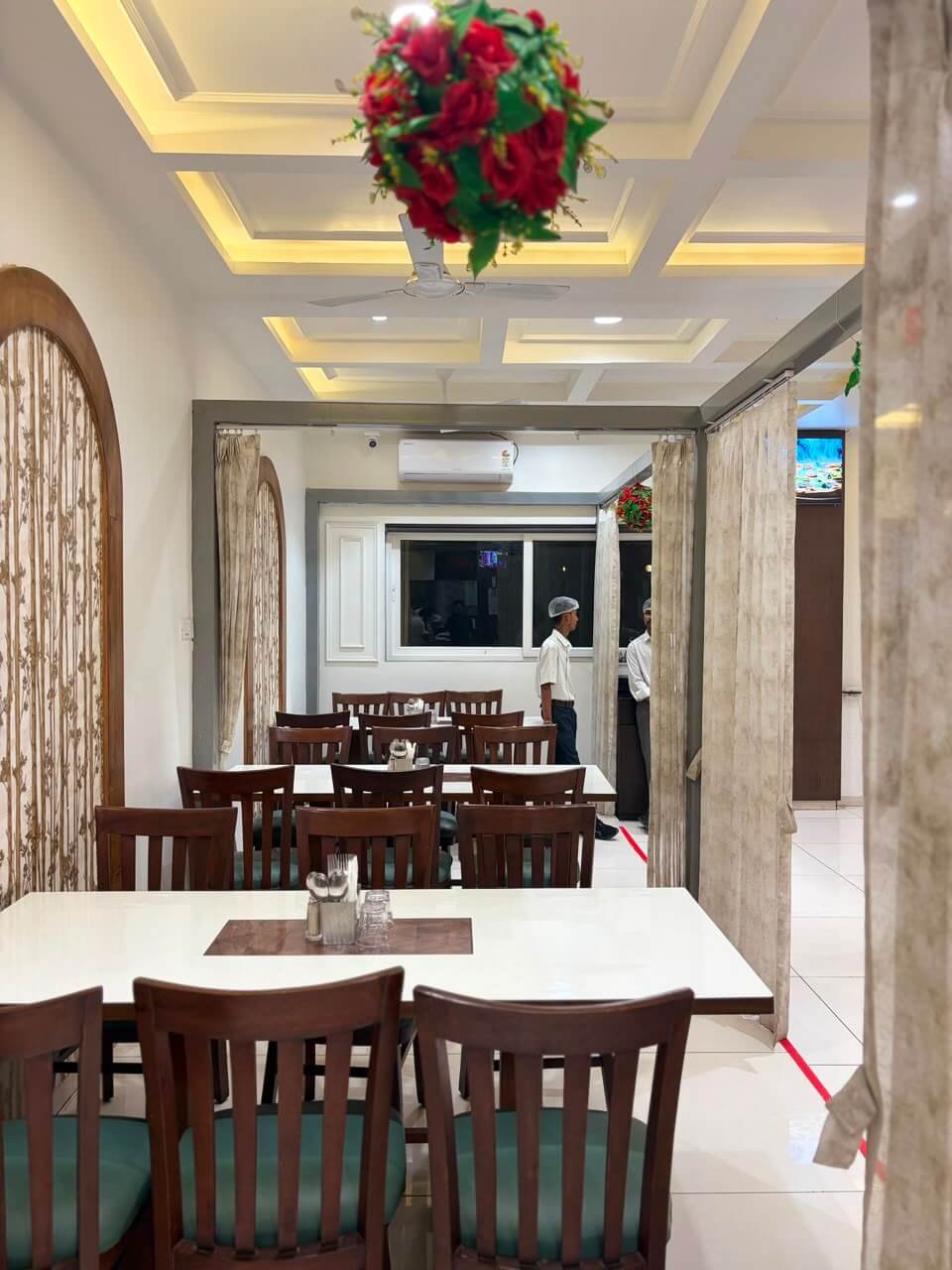 Restaurant interior in the evening with coffered ceiling, floral pendant and curtained partitions between dining sections