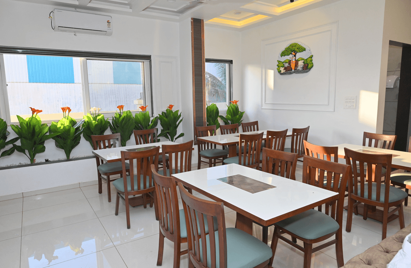 Pure vegetarian restaurant with wooden chairs, white tables and a planter of foliage beneath the windows