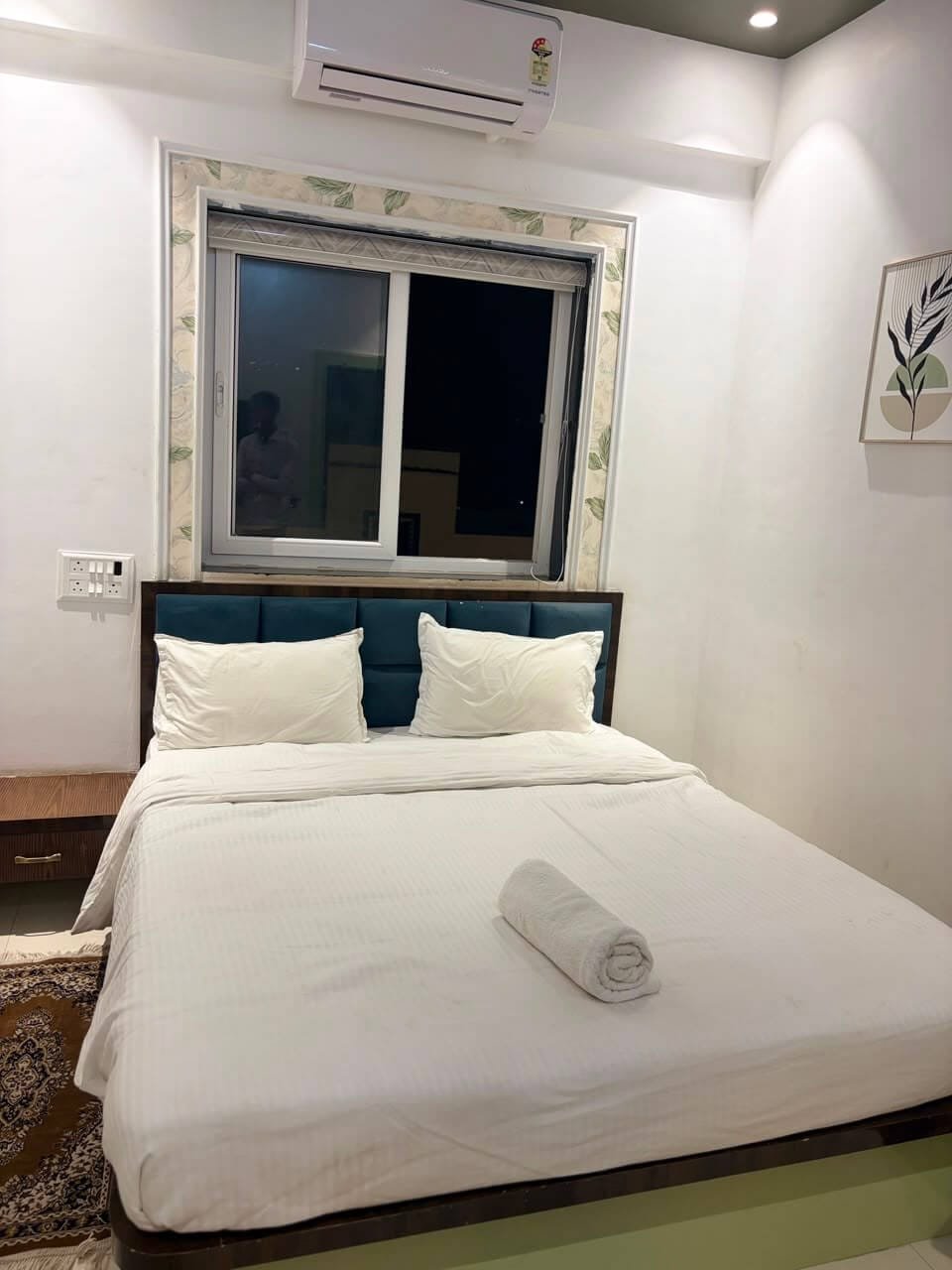 Guest room at night with the window open above the headboard, botanical print on the wall and a bedside drawer unit