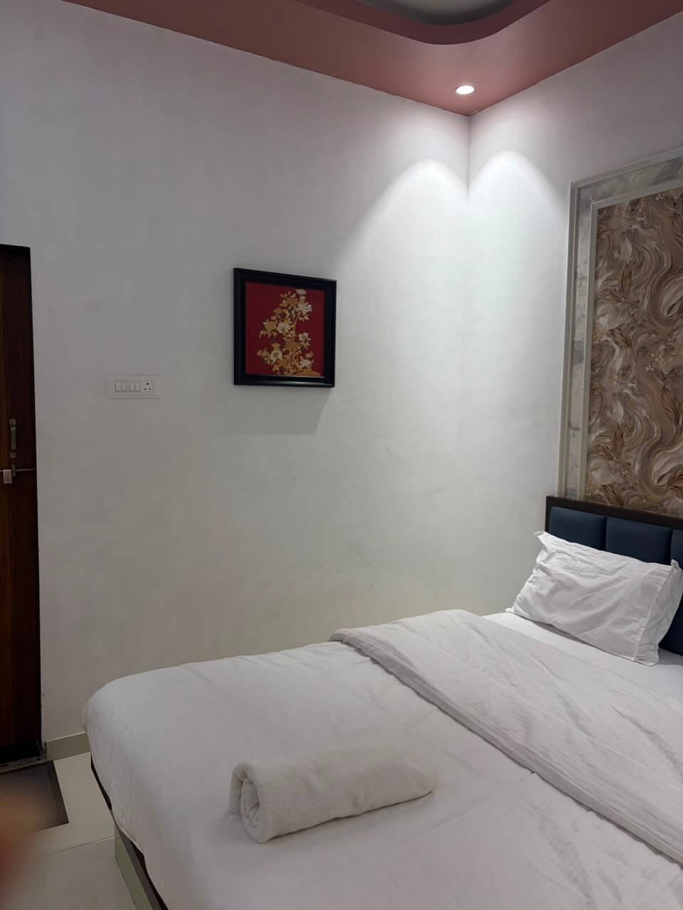 Bedside corner of a guest room with framed gold-on-red botanical artwork and accent downlighting