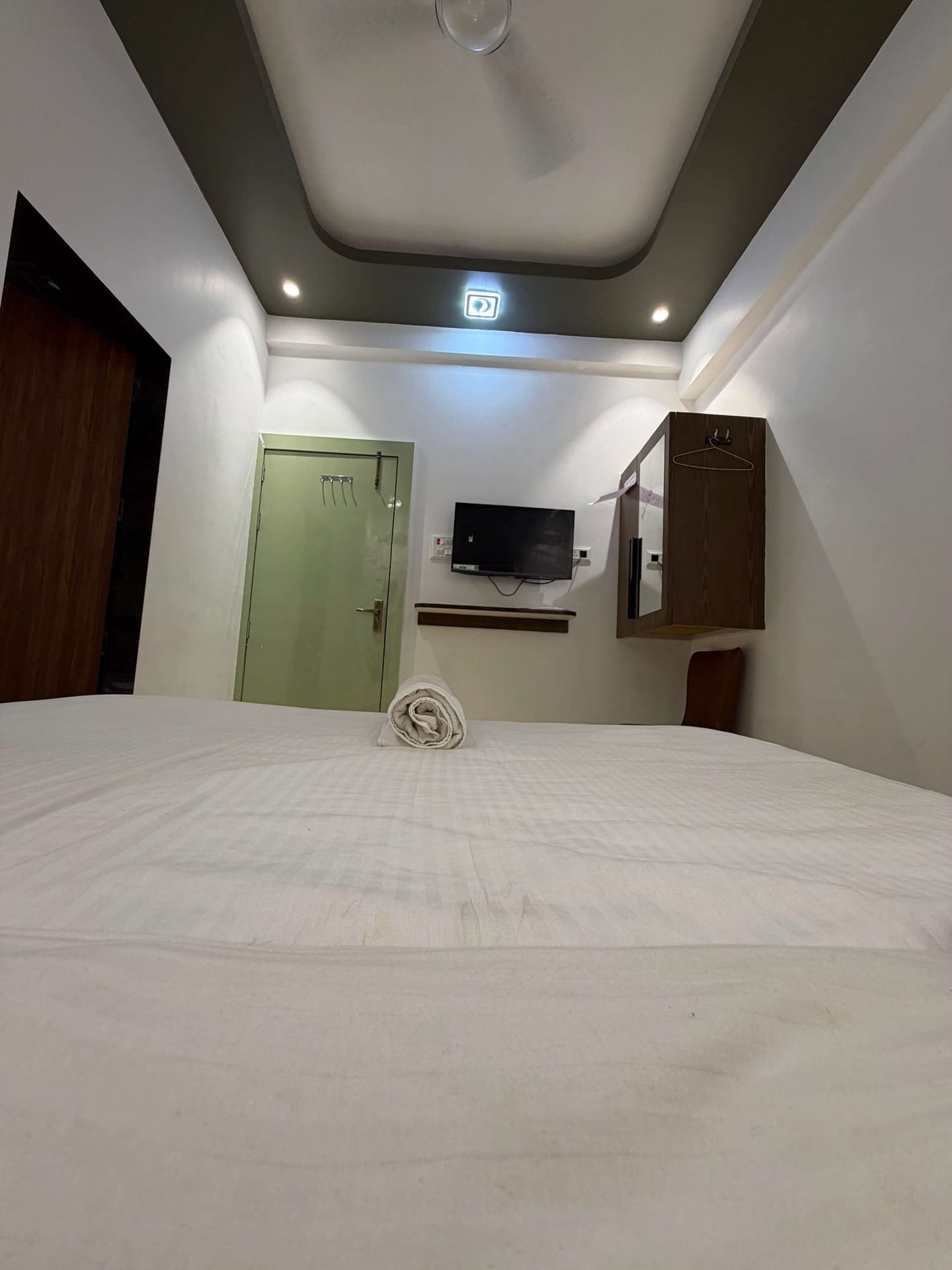 Compact guest room with a large bed, wall-mounted television, mirrored cabinet and bathroom door