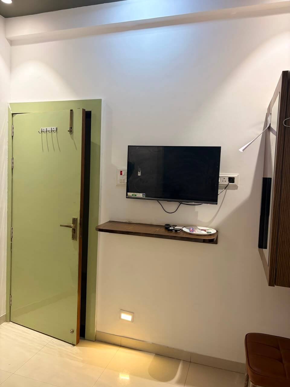 Room entry corner with a wall-mounted television on a timber shelf, coat hooks on the door and a wardrobe alongside