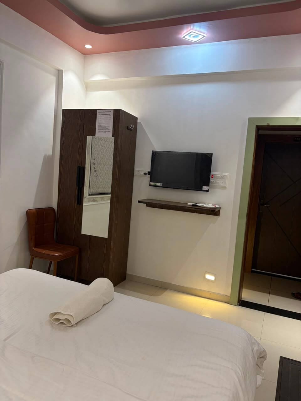 Room interior with tall wooden wardrobe, television on a wooden shelf and recessed cove lighting