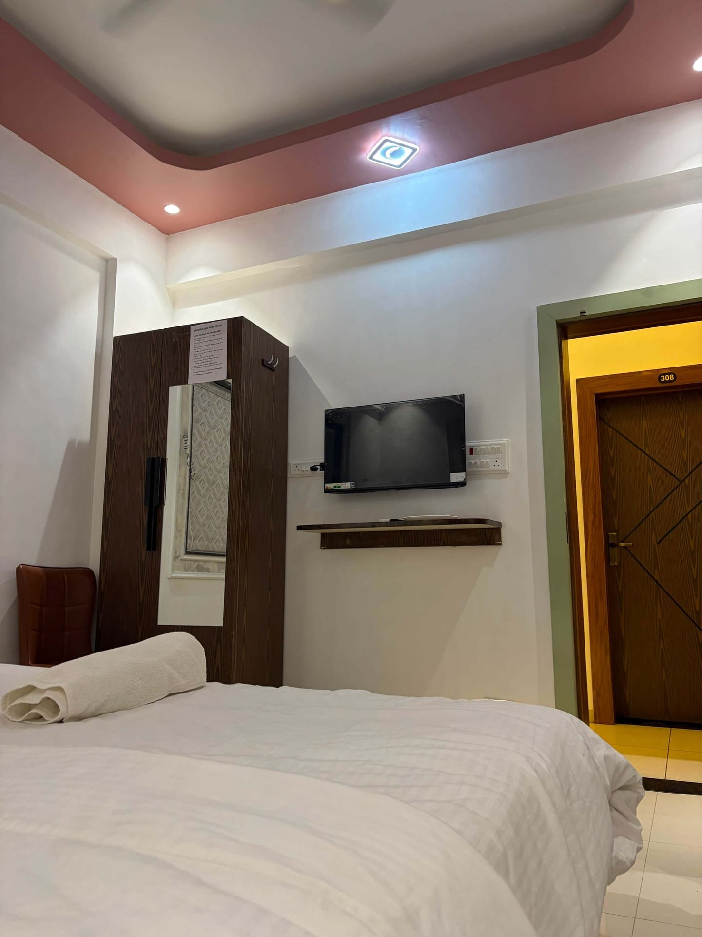 Guest room with wall-mounted flat-screen television, wooden wardrobe with mirror and the room door beyond